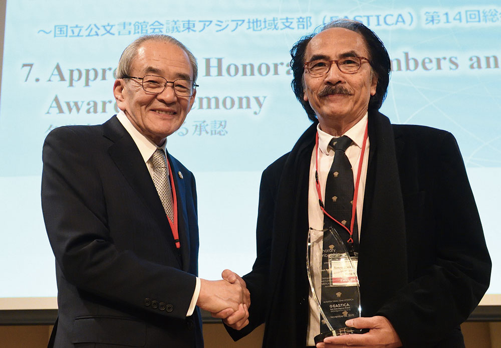 名誉会員の表彰を受けたサイモン・チュー氏(右)と握手する加藤丈夫国立公文書館長(左)